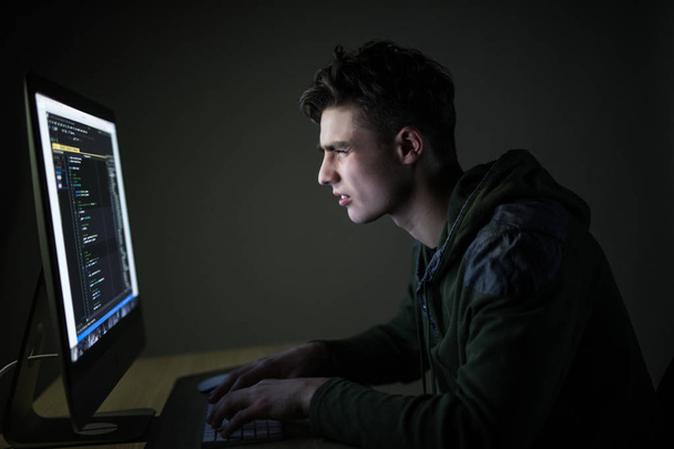 若い男が暗い部屋でハッキング サーバー。若者の暗い部屋でパソコンに programm コード。ホワイト ハッカー. - 写真・画像