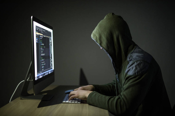 Um hacker em um capuz em um fundo escuro hackear redes de computadores no quarto escuro
 - Foto, Imagem