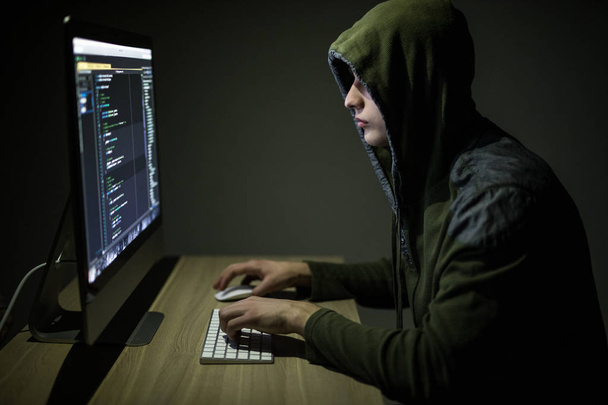 Mann mit Kapuzenpulli hackt Server im dunklen Raum. Junger Mann hackt Server oder weißen Hacker schützen Netzwerk - Foto, Bild