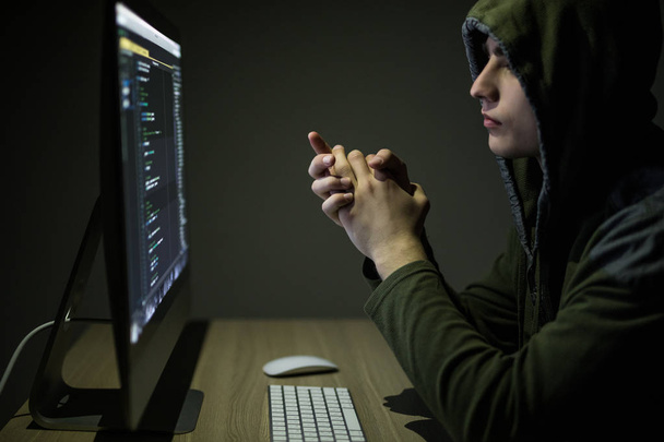 Man wearing hoodie hacking server in dark room. Young man hack server or white hacker protect network - Foto, afbeelding
