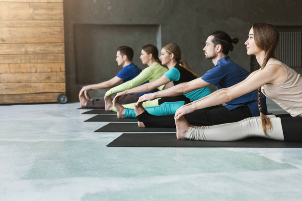Mujeres y hombres jóvenes en clase de yoga, haciendo ejercicios de estiramiento
 - Foto, imagen