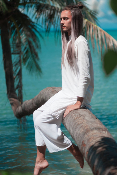 Handsome man is sitting on a palm tree - Zdjęcie, obraz