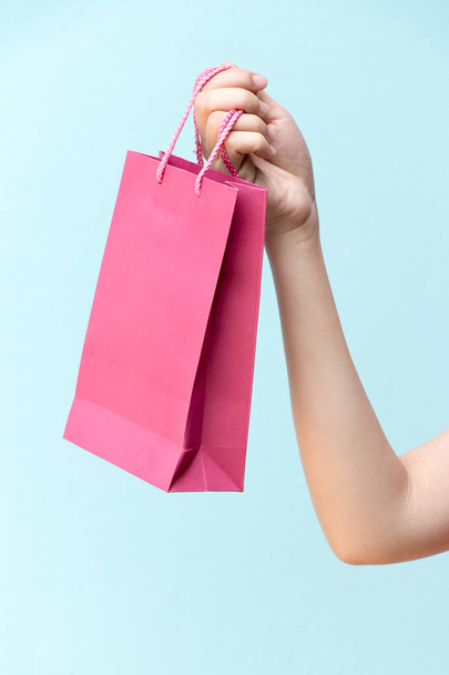 Рука бизнес-женщины держать розовый торговый мешок на синем бетонном фоне
 - Фото, изображение