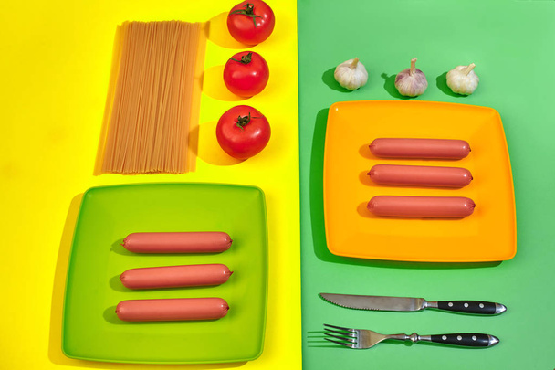 A lot of raw sausages on plate. On green and yellow background with pasta and vegetables, top view. - Foto, Imagem