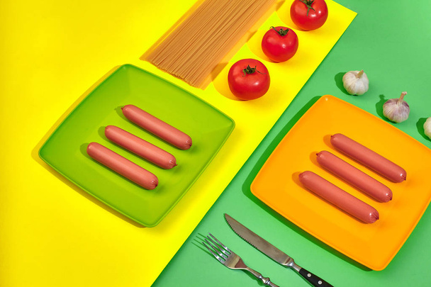 Un montón de salchichas crudas en el plato. Sobre fondo verde y amarillo con pasta y verduras, vista superior
. - Foto, Imagen
