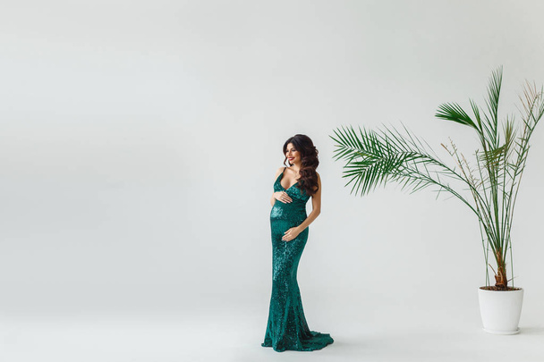 Beautiful future mother. Beautiful young pregnant woman in evening gown looking away with smile while standing against white background. - Photo, Image