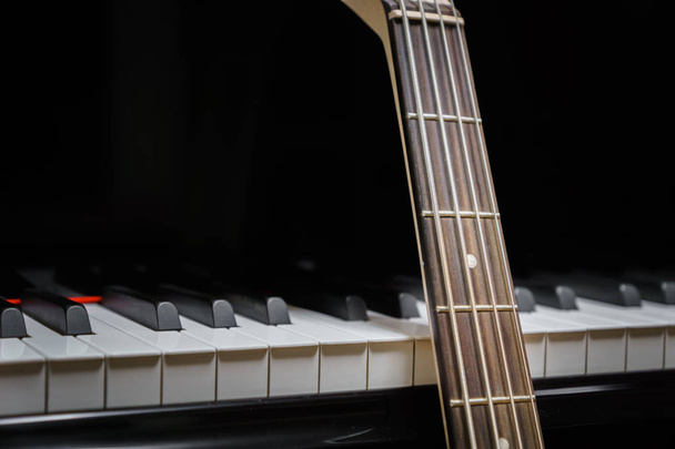 bass guitar against grand piano keys with plectrum - musical instruments closeup - concept musical composition and creativity - Photo, Image