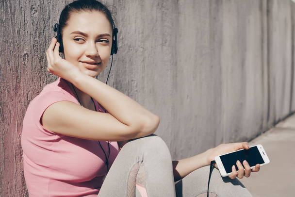 beautiful sports girl listening to music on headphones, resting after a hard workout outdoors - Zdjęcie, obraz