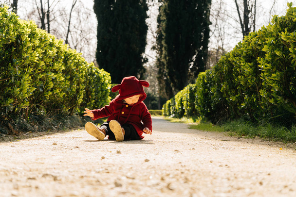 cute little baby boy in a funny suit sits on the ground in a park, exploring the world - Foto, Imagen