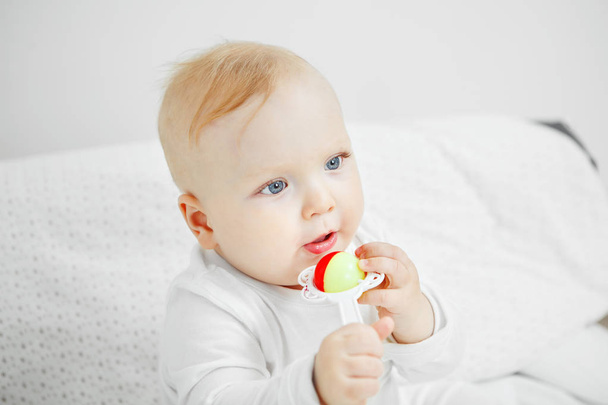 Cheerful baby sits on bed and holds rattle - Foto, afbeelding