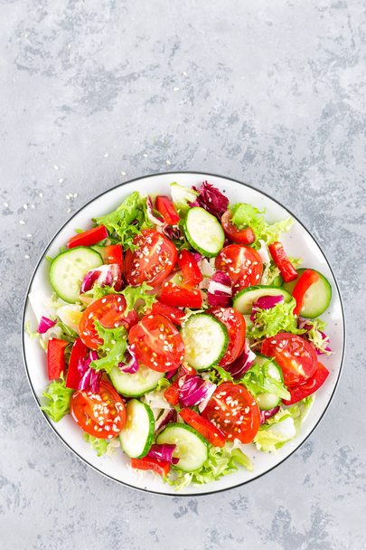 Fresh vegetable salad with tomatoes, cucumbers, sweet pepper and sesame seeds. Vegetable salad on white plate - Fotografie, Obrázek