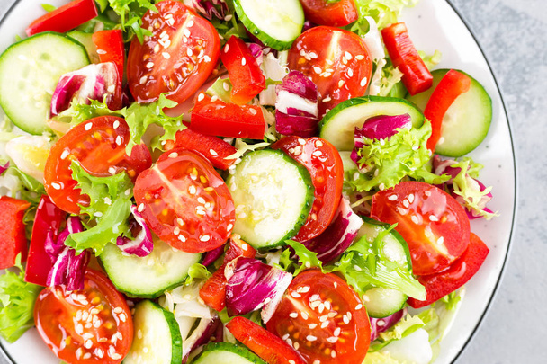 Fresh vegetable salad with tomatoes, cucumbers, sweet pepper and sesame seeds. Vegetable salad on white plate - Photo, Image