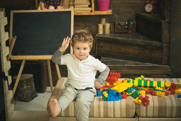 Koncepcja dzieciństwa. Chłopiec bawi się klockami budowlane w pokoju zabaw w pobliżu chalkboard. Boso dziecko siedzi na kanapie z kolorowe bloki z tworzyw sztucznych - Zdjęcie, obraz