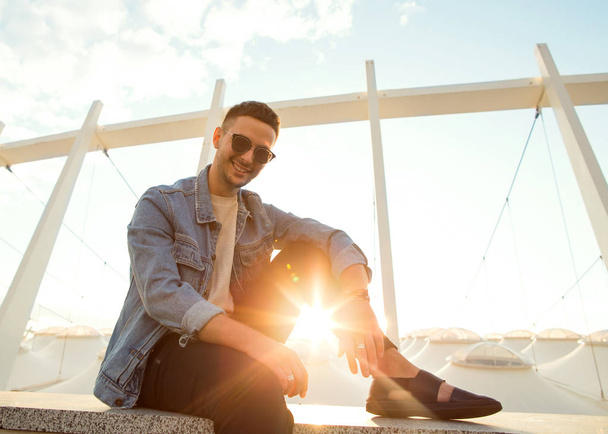 fashion guy sitting at sunset posing in sun glasses - 写真・画像