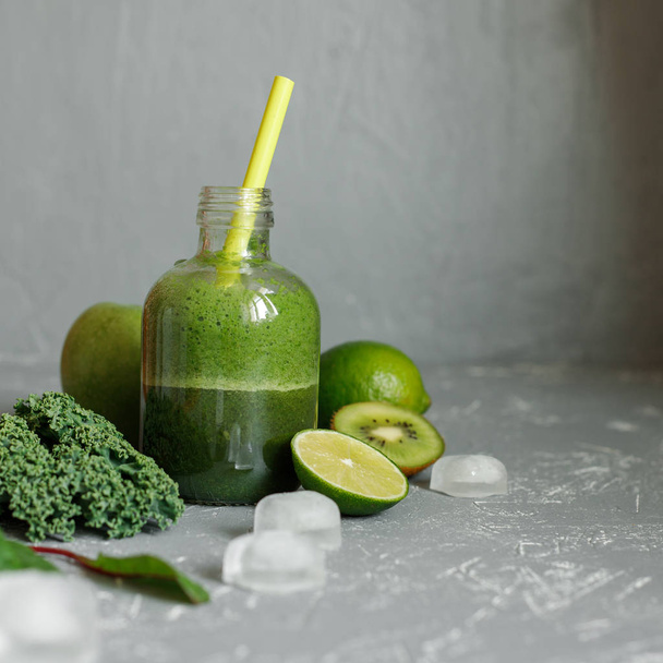 Smoothie verde saudável com ingredientes e cubos de gelo em fundo cinza
 - Foto, Imagem