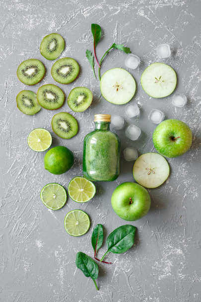 Здоровый зеленый смузи со свежими зелеными фруктами и листьями шпината на сером фоне, вид сверху
 - Фото, изображение