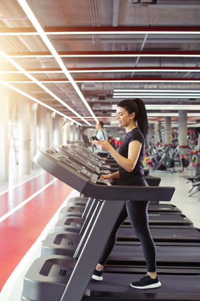 young Sportswoman using smartphone while jogging on treadmill - Foto, Imagen