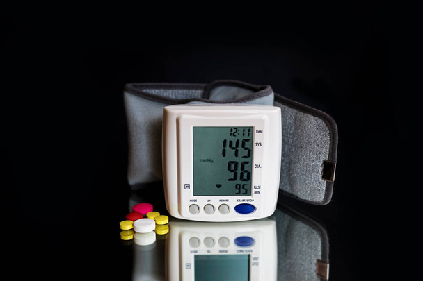 Fehér elektromos tonométer jelzi a vérnyomás. Orvostudomány, életkor, az egészségügy és emberek koncepció tonométer és tabletták, ami arra utal, hogy vigyázzon a vérnyomás. - Fotó, kép