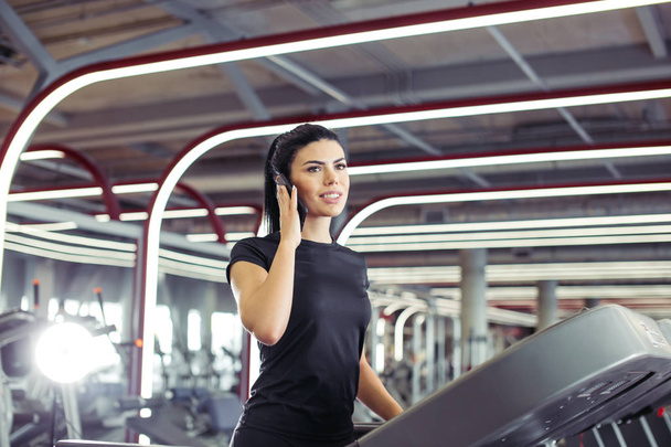 woman smiling while talking on mobile phone while running on treadmill - Foto, Bild
