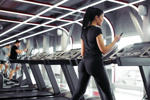 Sportswoman using smartphone for training workout app while jogging on treadmill - Fotografie, Obrázek