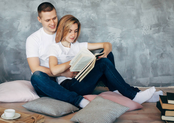 Genç iki katta oturan ve kitap okuma beyaz t-shirt içinde sevgi dolu. Uzay kopyalayın. Gri arka plan - Fotoğraf, Görsel