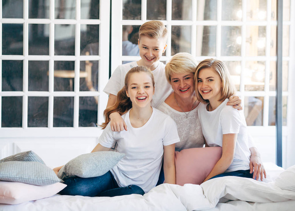 Rodzina Matka z synem i dwie córki baw, siedząc na łóżku obok okna w białe koszulki. Nieostrość - Zdjęcie, obraz