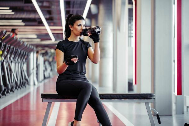 Fit woman with bottle using her smart phone with earphones in gym - Fotó, kép