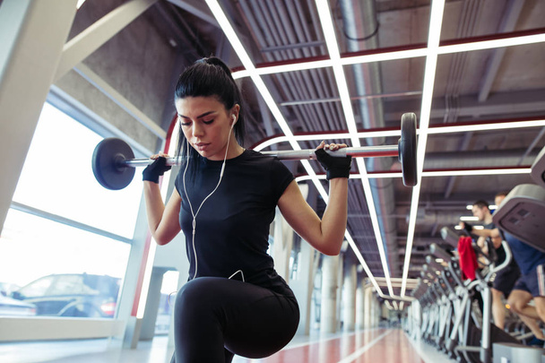 girl doing lunges with barbell in modern gym - Foto, afbeelding