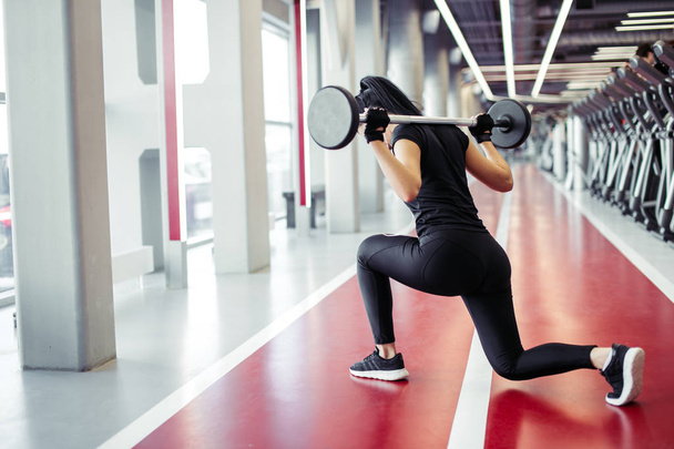 girl doing lunges with barbell in modern gym - Foto, imagen