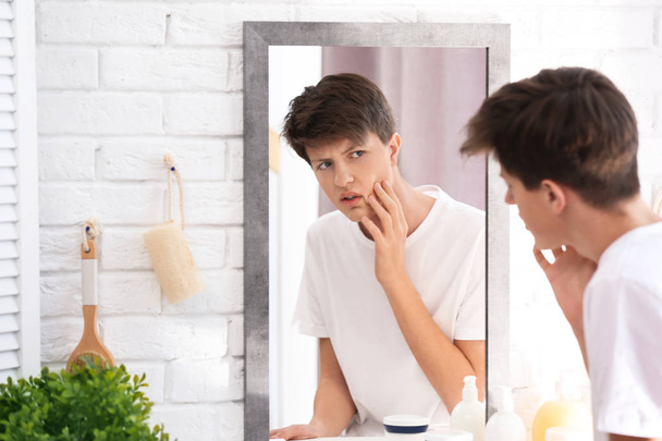 Teenage boy with acne problem looking in mirror at home - 写真・画像