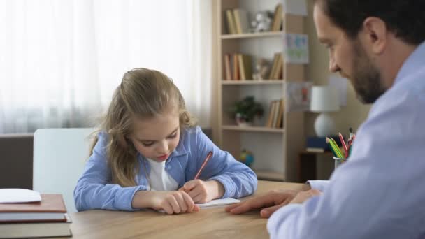 Glimlachend dochtertje zit aan tafel en huiswerk met vader, zorg - Video