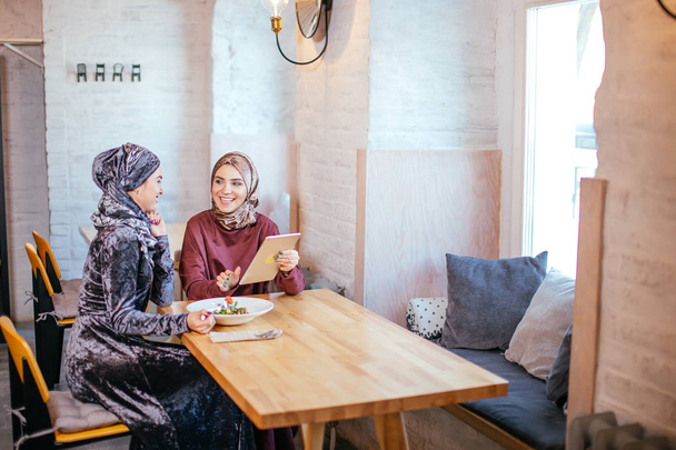Two Muslim women in cafe, shop online using electronic tablet - Foto, Imagen