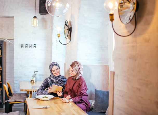 Deux femmes musulmanes dans un café, magasiner en ligne en utilisant une tablette électronique
 - Photo, image