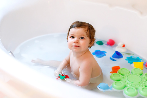 Χαριτωμένο αξιολάτρευτο κοριτσάκι που κάνει αφρόλουτρο στην μπανιέρα. Παιδικό παιχνίδι με παιχνίδια από καουτσούκ μπάνιου. - Φωτογραφία, εικόνα