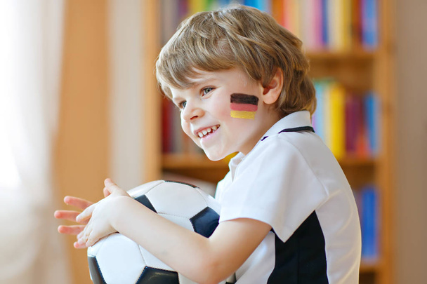 Little blond preschool kid boy with ball watching soccer football cup game on tv. - 写真・画像