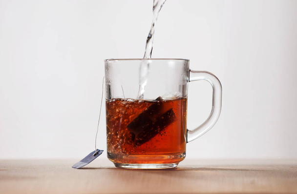 Boiling water is poured into a glass mug with a tea bag. Water turns into tea, it is painted in amber color. Front view - Фото, изображение