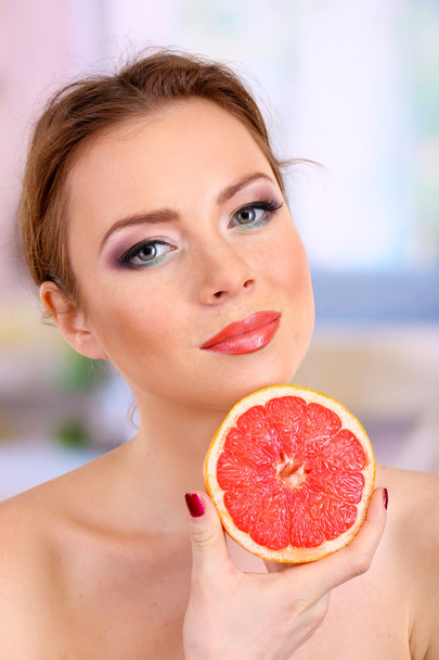 Beautiful young woman with bright make-up, holding grapefruit, on bright background - 写真・画像