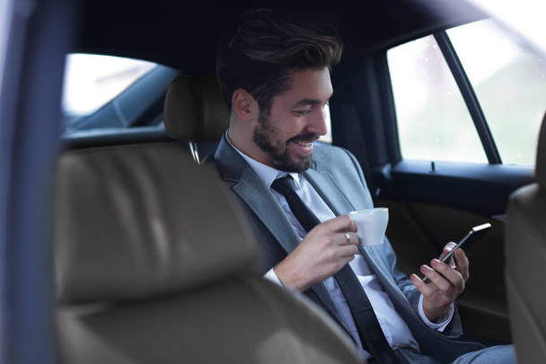 Businessman drinking coffee in car with phone in hand - Φωτογραφία, εικόνα