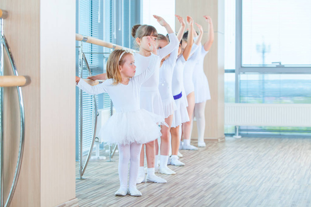 Young ballerinas rehearsing in the ballet class. They perform different choreographic exercises. They stand in different positions near the ballet barr. - Foto, Imagem