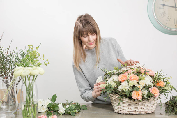 Smiling female florist. Floral workshop - woman making a beautiful flower composition a bouquet in a wicker basket. Floristry concept - Fotoğraf, Görsel