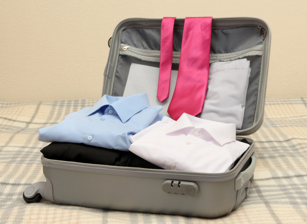Open grey suitcase with clothing on bed - Foto, Imagem