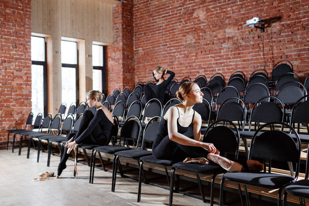 A balett koncepció. Fiatal balerina lány ül a fekete székek a teremben. A nők a próba, a fekete bodysuits. Készítsünk egy színházi előadás - Fotó, kép
