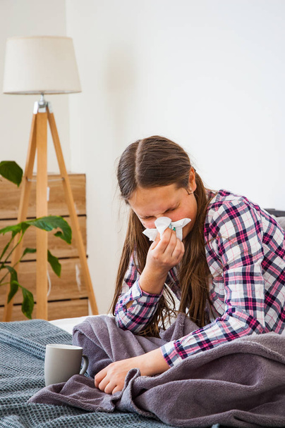 teenage girl is blowing her nose while sitting on a sofa. Headache. Virus. Medicines - Foto, Imagem