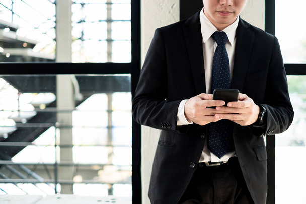 Young businessman standing with smartphone near the office window, business concept - Photo, image