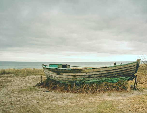 Vergaan vissersboot op oude droog gras. Verlaten houten schip met beschadigde motor  - Foto, afbeelding
