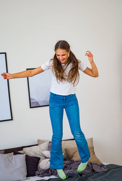 Teenager girl have fun jumping and dancing on bed in her room - Photo, Image