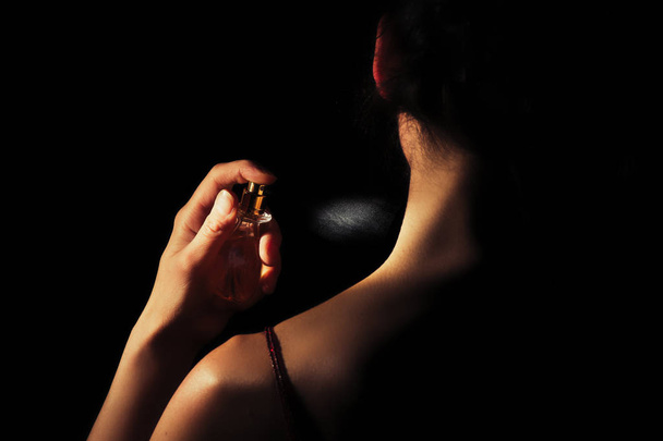 Woman sprays perfume on her neck with a black background - Fotoğraf, Görsel