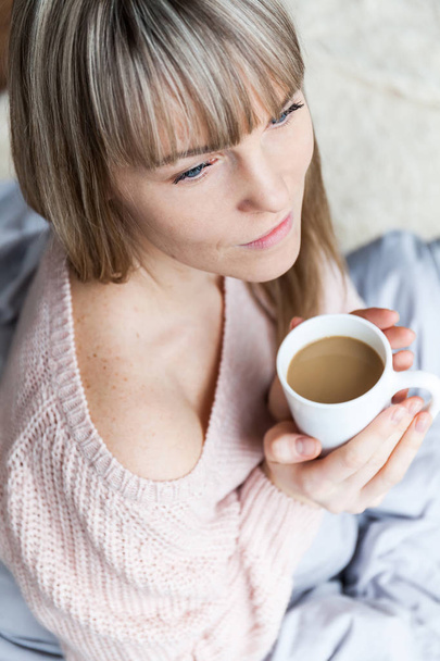 Красотка по утрам расслабляет женщину, а в постели пьет кофе. Кавказская молодая женщина расслабилась в постели с чашкой кофе
 - Фото, изображение