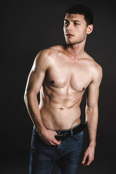 Pensive bare-chested man holding hands on belt - Foto, afbeelding