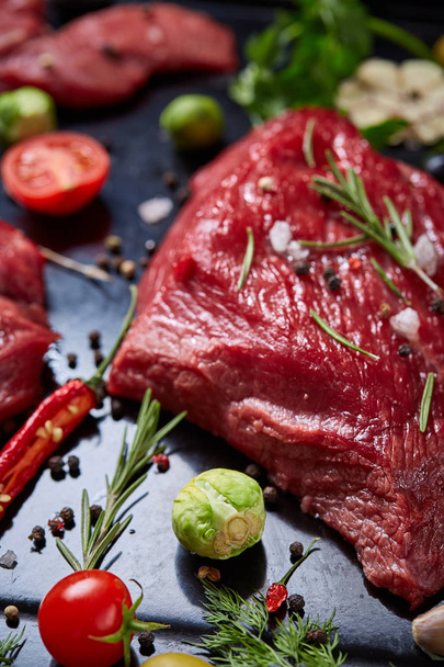 Flat lay of raw beefsteak with vegetables, herbs and spicies on metal tray, close-up, selective focus - Foto, afbeelding